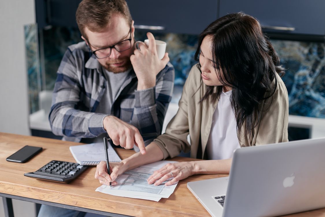 Casal analisando documentos financeiros à mesa, com calculadora, caderno e computador.