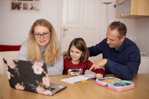 Dois adultos e uma criança reunidos à mesa com computador e cadernos, ilustrando a participação da família.