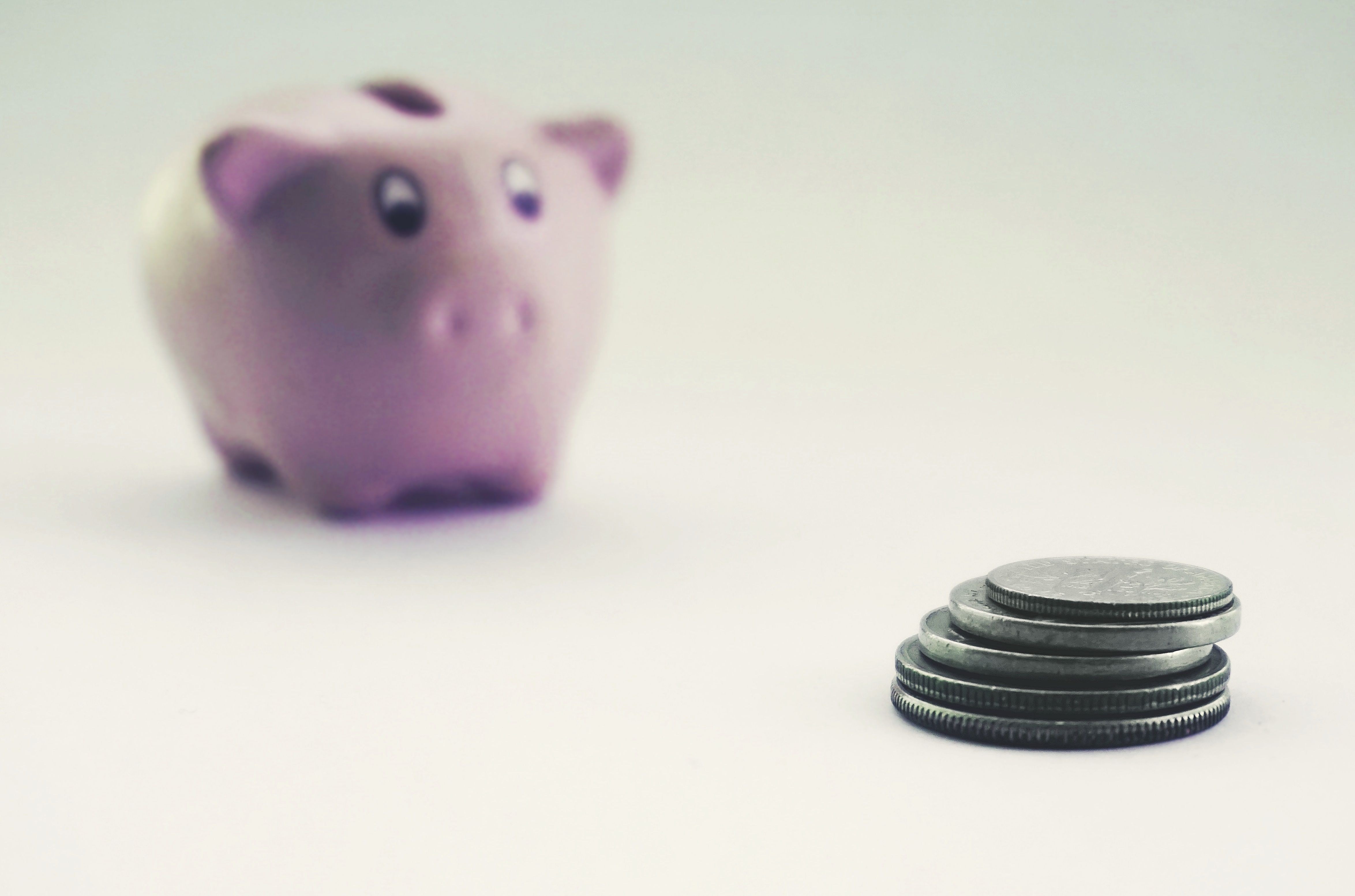 Pilhas de moedas com um cofrinho rosa desfocado ao fundo, ilustrando a economia para planos futuros.